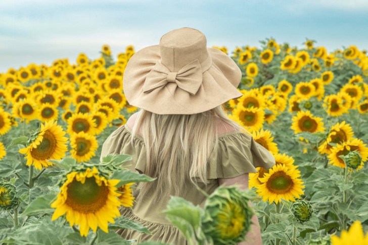 Žena v boho klobúku stojí v slnečnicovom poli