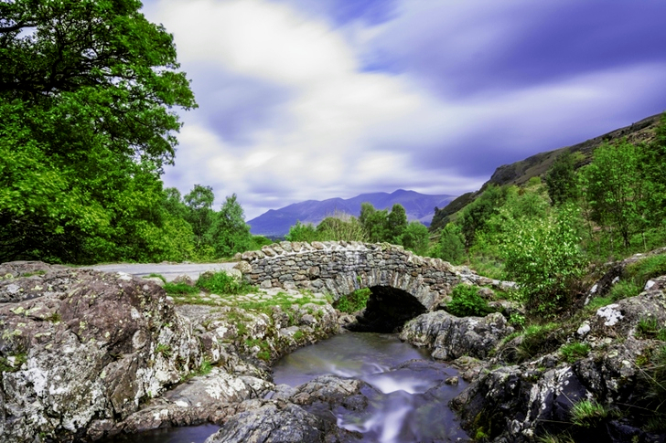 Grå klippeformation nær vand falder under overskyet himmel