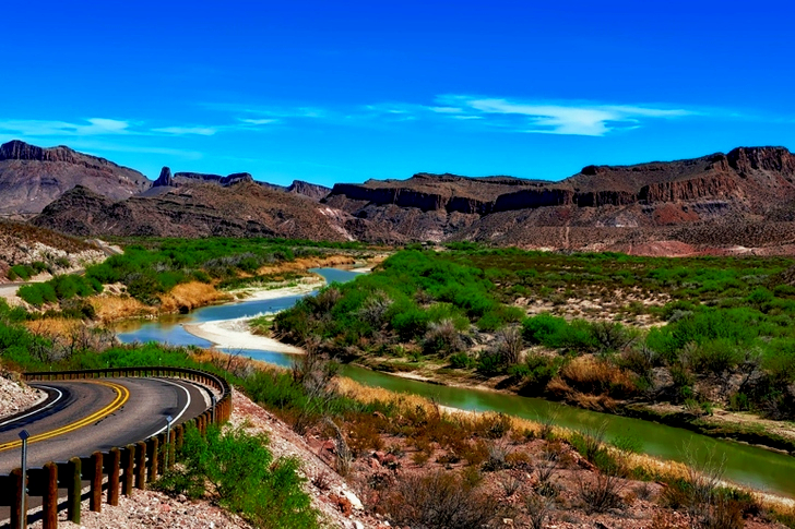 Black and Yellow 2 Way Road on Brown Mountain Surrounded by Green Trees Near Body of Water