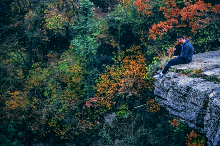 Man In Hoodie Sitting On Rock Cliff