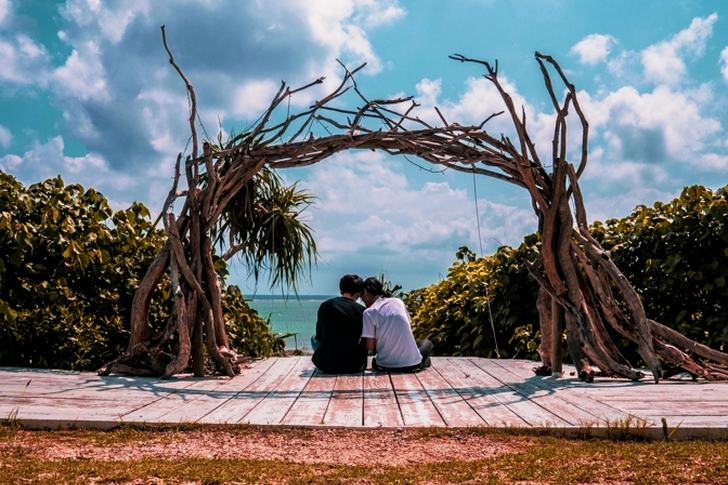 Man and Woman Sitting on Wooden Dock Under Cloudy Sky