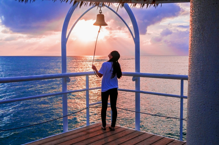 Woman Holding Rope With Bell Near Body of Water