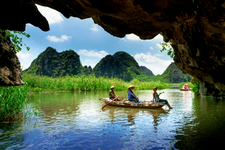 Three People Sitting on Boat While Sailing Under Cave