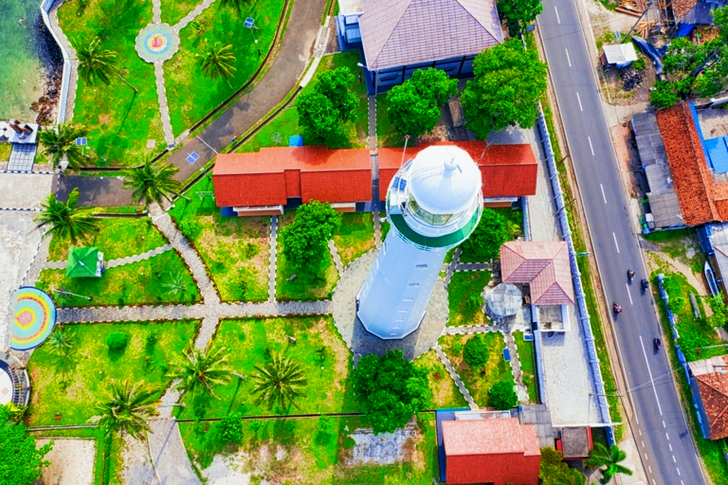 Aerial of White Lighthouse Near Multicolored Houses and Green Field View